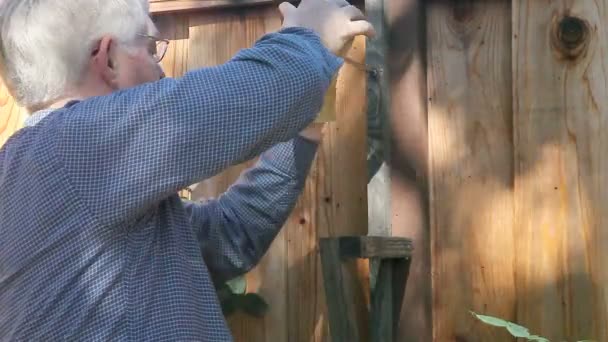 Starší muž používá šroubovák na dřevěné mříži proti plotu