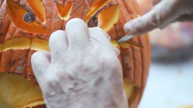 Bir adam jack o' fener yüzünün detaylarını kazımak için bıçak kullanır.