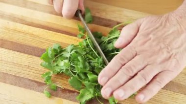 Yaşlı bir adam kesme tahtasında kişniş keser