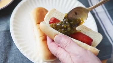 Yaşlı bir adam kağıt tabak üzerinde bir sosisli turşu çeşni kaşık