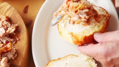 Bir adam mayonez ekler, tavuk çekti, coleslaw ve turşu bir börek topuzuna