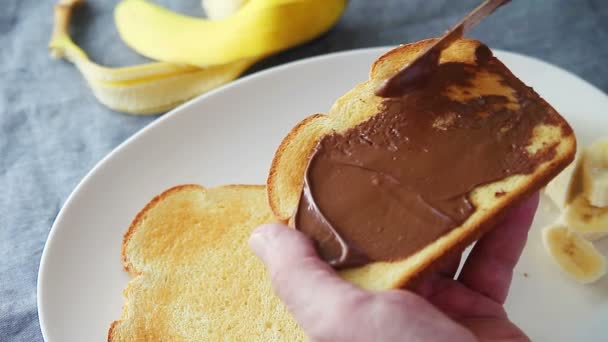 Een Man Zet Chocolade Hazelnoot Verspreid Toast Voegt Gesneden Bananen — Stockvideo