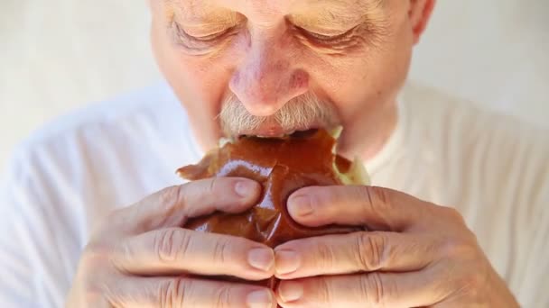 Yaşlı Adam Bir Börek Topuzun Üzerinde Bir Sandviç Içine Isırır — Stok video