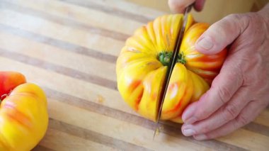 Bir adam doğrama tahtasında büyük, olgun bir domates keser