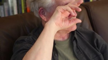 Yaşlı bir adam oturma odasında yorgun gözünü ovuşturuyor.