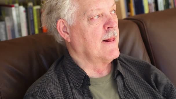 Entspannter Senior Auf Sofa Vor Bücherregal Spricht Und Amüsiert Sich — Stockvideo