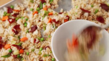 Bir kadın Çin sosis, havuç, bezelye ve soğan ile yapılan kızarmış pilav bir kase hizmet vermektedir