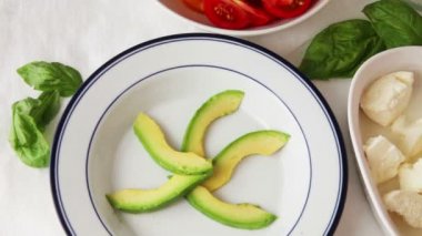 Bir kadın salata kasesinde avokado ve domates dilimleri, çeri domates, fesleğen ve burrata peyniri yerleştirir.