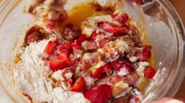 Bir kadın kek hamuru na taze çilek ekler ve malzemeleri karıştırır.