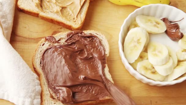 一个女人把香蕉和石榴种子在肉桂漩涡面包上覆盖着巧克力薄荷酱 — 图库视频影像