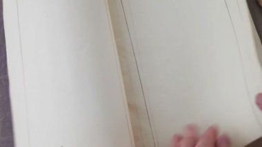 Bir kadın, kurallı çizgilerle antika bir kitabın sayfalarını çeviriyor. 