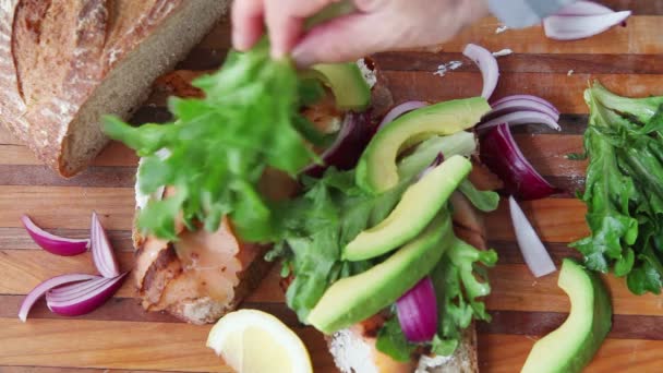 Una Mujer Prepara Sándwich Con Lechuga Aguacate Salmón Ahumado Cebolla — Vídeo de stock