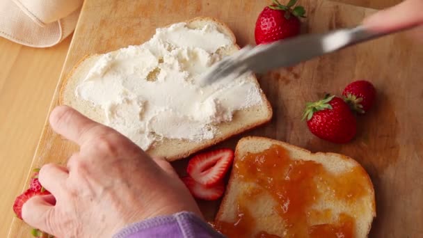 女性はパンに広がるクリームチーズに新鮮なイチゴを置きます — ストック動画