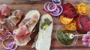 Bir kadın kesme tahtasında et ve sebzeli sandviç yapar.