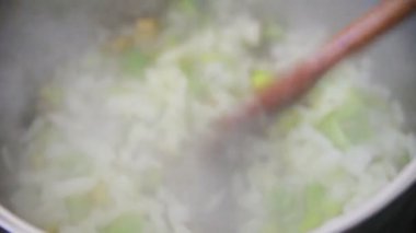 Bir kadın bir tavada doğranmış sebze pişirir, kısmen buhar tarafından gizlenmiş