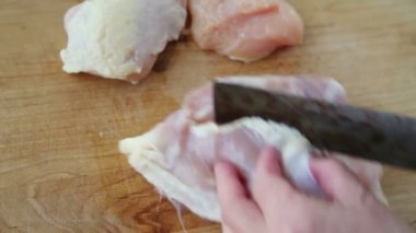 Bir kadın tavuk etini kemikten kesiyor.