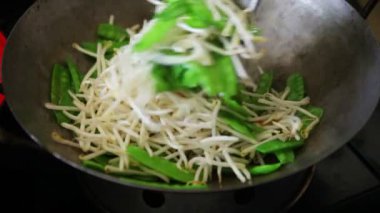 Bir kadın bir wok kar bezelye taze fasulye filizi ekler