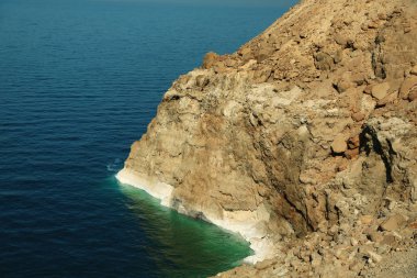 Kayalık sahil, Dead Sea Ürdün Haşimi Krallığı içinde. Yeşil su ve sarı kayada beyaz tuz yatakları
