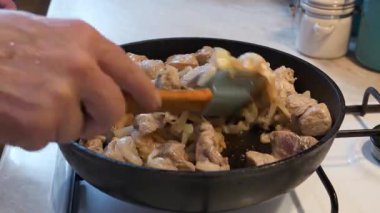 Kızarmış et. Aşçı, et parçalarını soğanla karıştırıyor. Gaz ocağında kızartma tavasında.