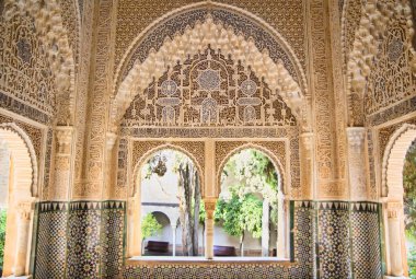Moorish architecture in one room of the Nasrid Palaces of the Alhambra of Granada in Spain, with beautiful intricate carvings and windows overlooking a garden. clipart