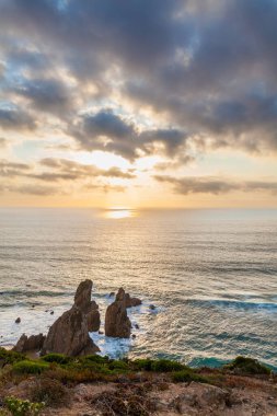 Praia da Ursa 'nın dramatik bir sahnesi. Yükselen deniz yığınları, engebeli uçurumlar ve gün batımında altın renkli gökyüzünün altında yemyeşil bir yer.