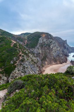 Engebeli uçurumlar ve yemyeşil tepeler arasında uzanan tenha kumlu bir sahil, yumuşak bir gökyüzünün altında yüksek bir görüş açısına sahipti.