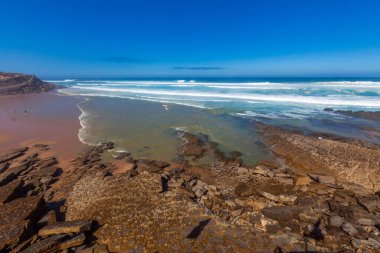 Beyaz binaları, terakotta çatısı, saksı bitkileri ve canlı çiçekleri olan sakin bir avlu berrak mavi gökyüzünün altında manzaralı bir okyanus manzarasına götürür.