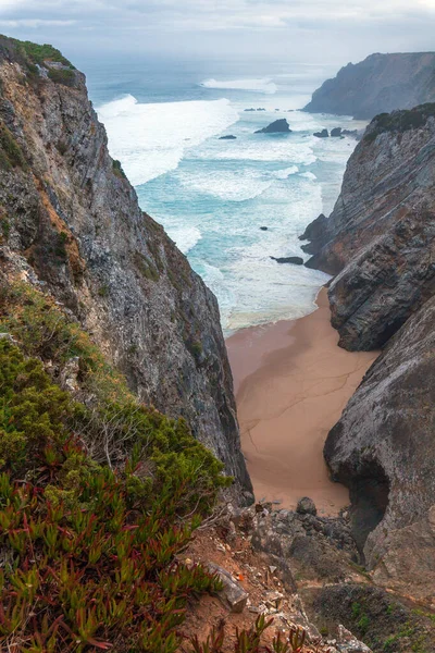 Beyaz binaları, terakotta çatısı, saksı bitkileri ve canlı çiçekleri olan sakin bir avlu berrak mavi gökyüzünün altında manzaralı bir okyanus manzarasına götürür.
