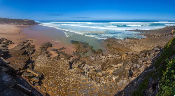 Turkuaz dalgaların kayalık bir sahile çarptığı çarpıcı bir sahil sahnesi, Apple sahilinde canlı mavi bir gökyüzünün altında kumlu kumsalla buluşması.