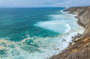 Sessiz bir kıyı yolu yemyeşil bitki örtüsü ve uzun kamışların arasından Atlantik Okyanusu 'ndaki açık mavi gökyüzünün altına doğru uzanır.