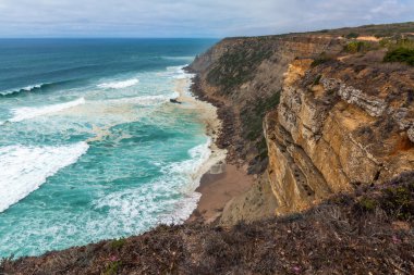 Sessiz bir kıyı yolu yemyeşil bitki örtüsü ve uzun kamışların arasından Atlantik Okyanusu 'ndaki açık mavi gökyüzünün altına doğru uzanır.