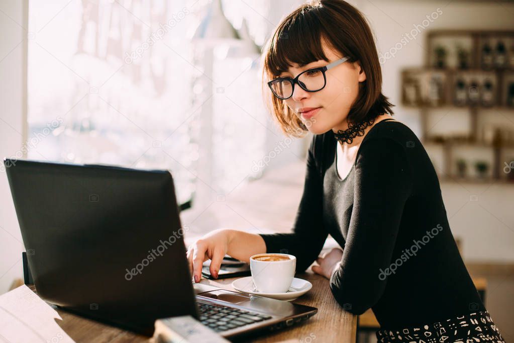 Smiling young woman using laptop in the cafe. Female working on laptop in an indoor cafe.