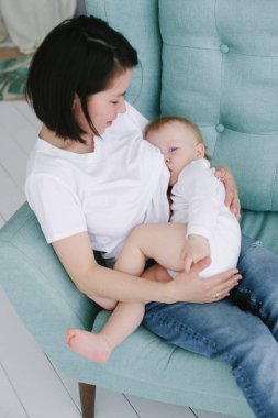 Genç anne yatak odasındaki kanepede oturur ve bir yaşındaki bebeğini emzirir.