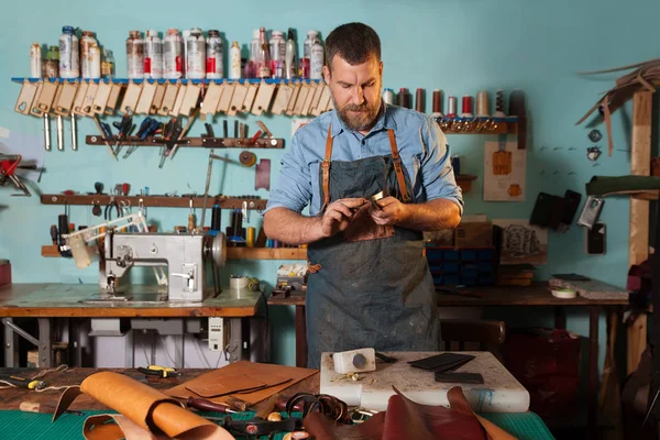 El hombre trabaja en un estudio de fabricación de bolsas. Sastre en delantal trabajando con cuero en taller . — Foto de Stock