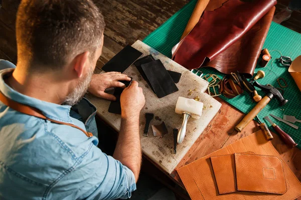 Hombre trabajando con cuero usando herramientas de artesanía . — Foto de Stock