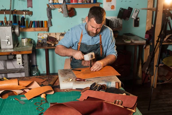 Artesano de cuero que trabaja con cuero natural usando martillo. Maestro de bolsos en el trabajo en taller local. Concepto hecho a mano . — Foto de Stock