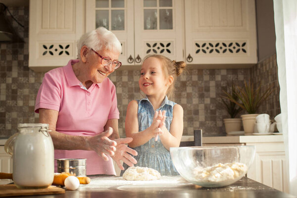 Cute little girl and her grandmother cooking on kitchen.