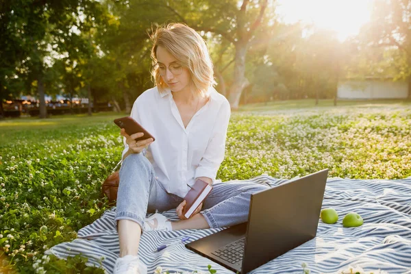 Молодая Женщина Сидящая Лужайке Парке Пользуется Ноутбуком Смартфоном — стоковое фото