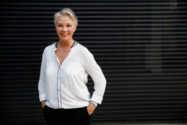 Güzel orta yaşlı iş kadını elinde bir fincan kahveyle siyah duvara poz veriyor..