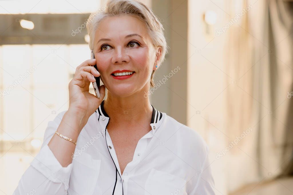 Beautiful stylish middle aged woman with gray hair uses smartphone