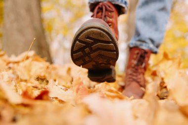 Sonbahar yaprakları üzerinde yürüyen ayaklar. Dışarıda, yakın plan.