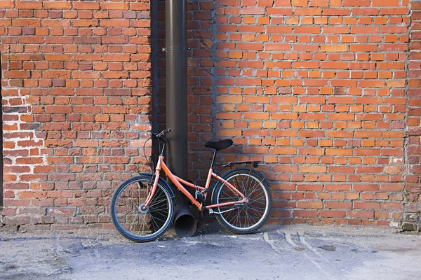 One parked bicycle against the background of an old brick wall fastened to the rainwater leader (pipe) in a city.
