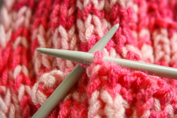 A pair of grey plastic knitting needles and pink wool yarn, knitted scarf.