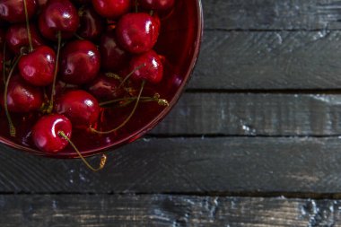 Siyah ahşap tahta masa arka plan üzerinde kırmızı cam bir kase taze, olgun kiraz . Kopyalama alanı yla yukarıdan görüntüle