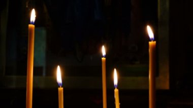 İnce kilise mumları yüksek çözünürlüklü 4k karanlıkta kutsal görüntülerin yakınında bir Ortodoks Hıristiyan kilisesinde yakmak