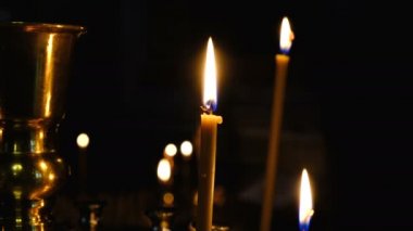İnce kilise mumları yüksek çözünürlüklü 4k karanlıkta kutsal görüntülerin yakınında bir Ortodoks Hıristiyan kilisesinde yakmak