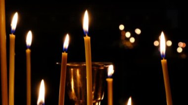 İnce kilise mumları karanlık yakın çekimde kutsal görüntülerin yakınında bir Ortodoks Hıristiyan kilisesinde yakmak, yakınlaştırma ve kamera hareketli kullanılarak filme