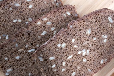 Kesme tahtasının üzerinde duran dilimlenmiş ayçekirdeği ve siyah çavdar ekmeğinin yemek arka plan makrosu fotoğrafı.