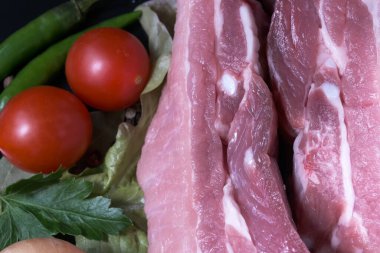 Çiğ domuz eti, sebzelerle, otlarla ve baharatlı baharatlarla kaplanmış siyah arka plan makro fotoğrafı.