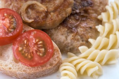 Lezzetli taze et pirzolası soğanla kızartılmış sığır eti, domuz eti ve tavuğun karışımı. Bir dilim beyaz ekmek ve beyaz tabak üzerinde makarna olan bir domates.